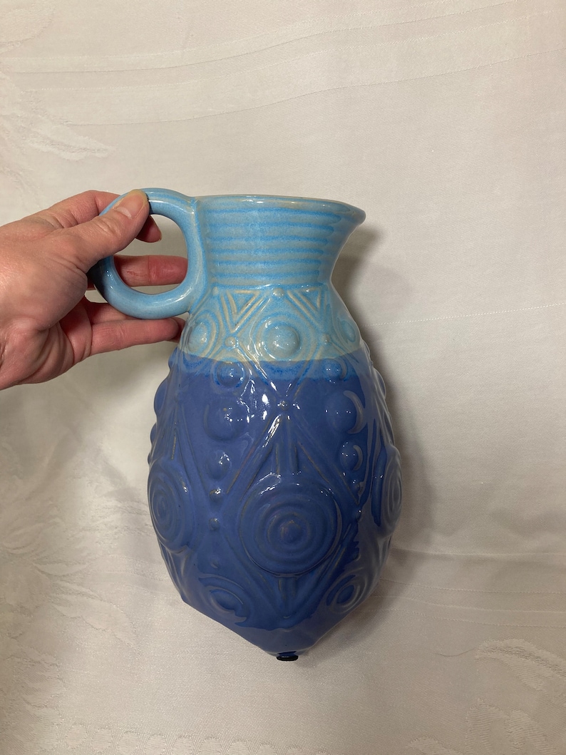 May include: A blue and light blue ceramic pitcher with a textured design. The pitcher has a rounded body and a handle.