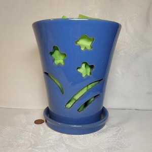 May include: A blue ceramic planter with a decorative design of stars and grass. The planter has a matching saucer.