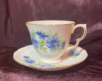 May include: A white teacup and saucer with a blue floral pattern. The cup and saucer have a gold trim around the edges.