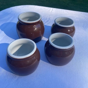 May include: Four small brown ceramic pots with white rims. The pots are arranged on a white tablecloth.