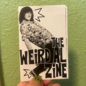 Peut inclure: Un fanzine noir et blanc intitulé "The Weird Al Zine" avec une photo de "Weird Al" Yankovic. Le fanzine présente une image en noir et blanc de Yankovic dans une chemise à motifs et un pantalon noir. Le fanzine est tenu sur un fond vert.