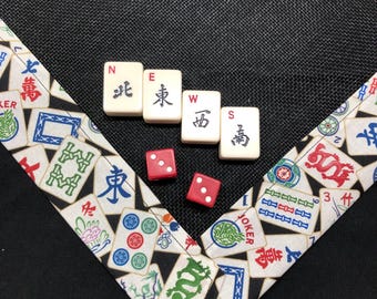 Może przedstawiać: Czarna powierzchnia z tkaniny z trójkątną obwódką w motyw płytek Mahjong. Cztery kremowe płytki Mahjong ułożone są w litery N, E, W, S z czarnymi znakami. Obok leżą dwie małe czerwone kostki do gry z białymi oczkami na każdej ze ścianek.