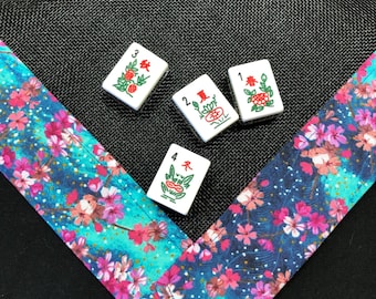May include: Four white mahjong tiles with green and red Chinese characters and symbols on a black background with a blue and pink floral border.