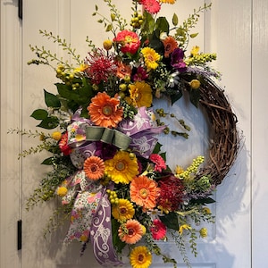 May include: A spring-themed wreath with a variety of flowers in shades of yellow, orange, pink, and red. The wreath is decorated with a purple and white ribbon with a butterfly design.