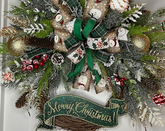 May include: A green and brown Christmas wreath with a burlap bow, pine sprigs, red berries, gold ornaments, and a sign that says "Merry Christmas!"
