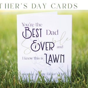 Op de afbeelding: Een witte kaart met een paars en gouden ontwerp met de tekst "You're the BEST Dad EVER and I know this is LAWN" met een tekening van een grasmaaier. De kaart ligt op groen gras.