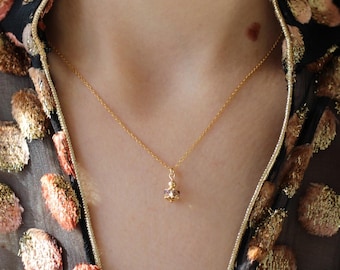 May include: A delicate gold chain necklace featuring a small, round, faceted pendant with a metallic finish. The pendant is suspended from a thin, polished gold-tone link chain that rests against the neck, showcasing a simple and refined design.