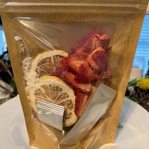 May include: A clear plastic bag filled with dried fruit and citrus slices. The bag is made of brown paper and has a zipper closure. The fruit is red and the citrus slices are yellow.