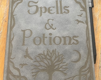 May include: A gray leather-bound journal with the words "Spells & Potions" embossed on the front cover. The cover features an intricate design of trees and a crescent moon.