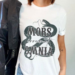 May include: White t-shirt with a black snake graphic and the text "MORS irrumat OMNIA".