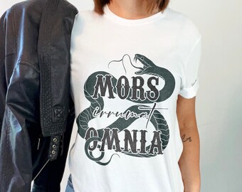 Puede incluir: Camiseta blanca con un gráfico de serpiente negra y el texto "MORS irrumat OMNIA".