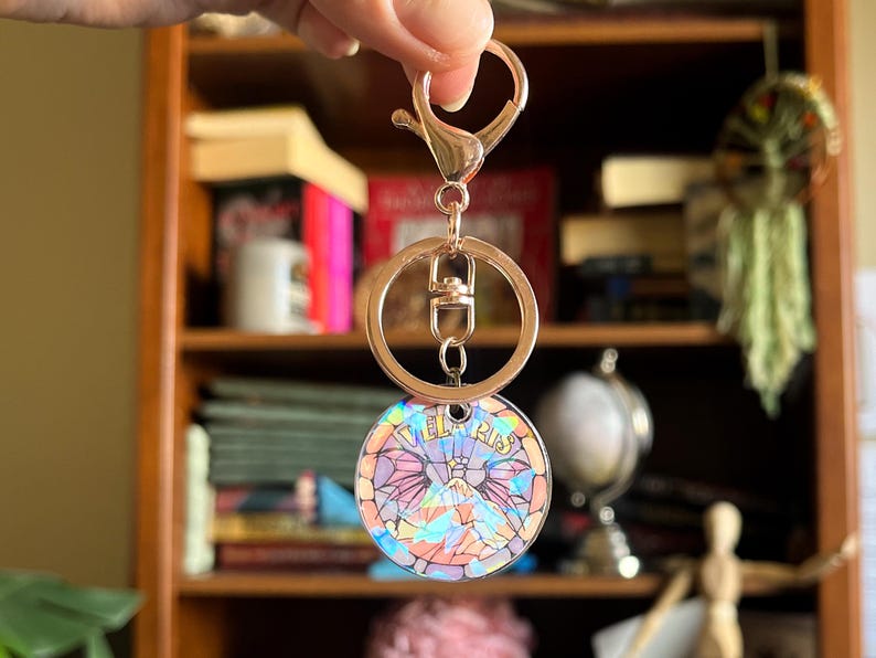 Op de afbeelding: Een gouden sleutelhanger met een ronde, iriserende hanger met een berglandschap en de tekst "Tel Aviv".