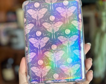 May include: A clear phone case with a holographic iridescent finish. The case features a repeating pattern of white moth silhouettes on a dark background.