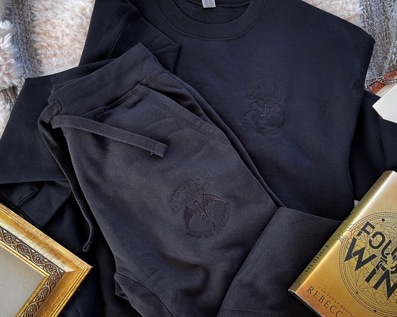 K&ouml;nnte beinhalten: Schwarze Jogginghose und ein schwarzer Pullover mit einer Grafik eines Vogels und dem Text "For The Glory Of The Underworld".