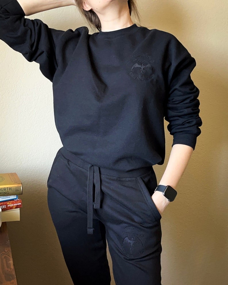 K&ouml;nnte beinhalten: Schwarzer Pullover und Jogginghose mit einem schwarzen gestickten Design eines Vogels mit dem Text "Theology of the Birds" auf der Vorder- und R&uuml;ckseite.