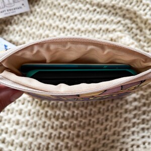 May include: A small zippered pouch with a floral print and a light brown lining. A teal and black electronic device is inside the pouch.