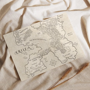 May include: A detailed map of Erilea, featuring geographical regions such as the Frozen Wastes, Western Wastes, and Deserted Lands. The map is printed on a beige paper with a compass rose and decorative lettering. Two stalks of wheat are in the foreground.