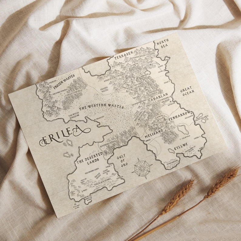 May include: A detailed map of Erilea, featuring geographical regions such as the Frozen Wastes, Western Wastes, and Deserted Lands. The map is printed on a beige paper with a compass rose and decorative lettering. Two stalks of wheat are in the foreground.