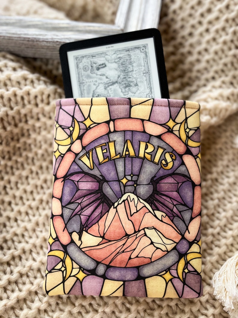May include: A yellow, purple, and pink stained glass pattern e-reader cover with the word "Velaris" in gold lettering. The design features a mountain range and a crescent moon.