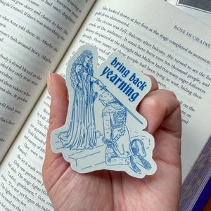 May include: A blue and white sticker featuring a medieval-style illustration of a kneeling figure and a woman holding a sword. The sticker has the text "bring back yearning" in a blue, uppercase font.
