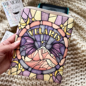 May include: A stained glass style e-reader cover with a purple, pink, and yellow design. The cover features a mountain range with a crescent moon and stars. The text "VELARIS" is written in gold lettering.