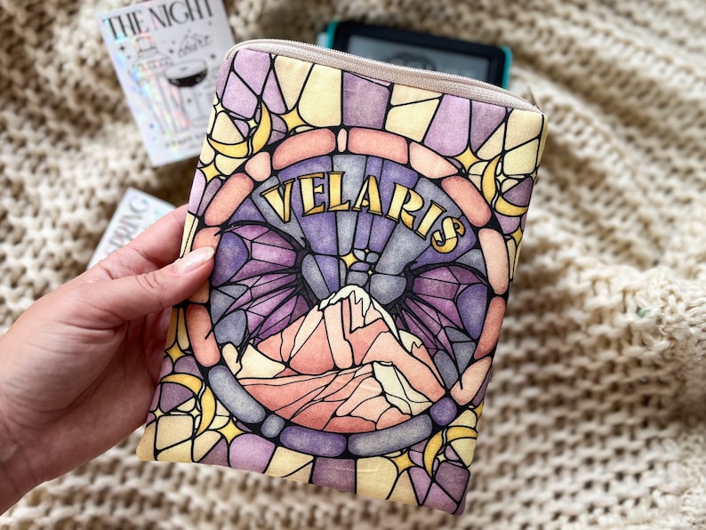 May include: A stained glass style e-reader cover with a purple, pink, and yellow design. The cover features a mountain range with a crescent moon and stars. The text "VELARIS" is written in gold lettering.