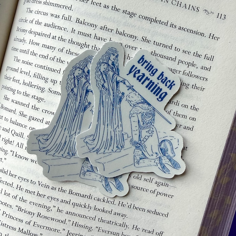 May include: Three stickers with a blue line drawing of a medieval scene. The stickers are on a book. One sticker has the text "bring back yearning". The scene depicts a kneeling figure and two figures in long gowns.