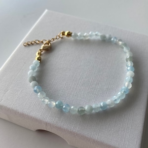 May include: A delicate bracelet made with light blue aquamarine beads and a gold clasp.
