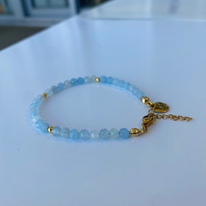 May include: A delicate bracelet made with light blue gemstone beads and gold accents. The bracelet has a clasp closure.