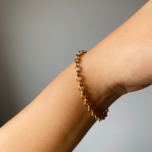 May include: A gold chain bracelet with a delicate, linked design. The bracelet is worn on a person's wrist.