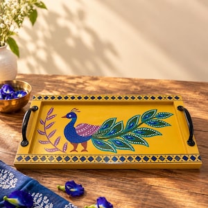 Puede incluir: Una bandeja de servicio rectangular amarilla con un pavo real pintado a mano con plumaje azul, verde y morado. La bandeja incluye dos asas de metal negro en los laterales y un borde geométrico decorativo azul y amarillo en los extremos.