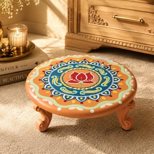 May include: A round, low-profile wooden stool with a light orange base color. The top surface features a detailed, multi-colored mandala pattern in shades of teal, white, and yellow, centered with a red lotus flower design on four curved legs.