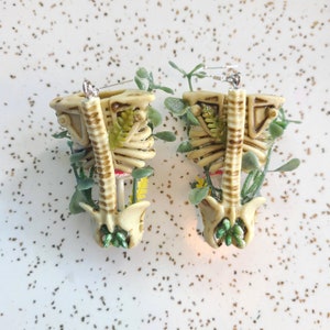 Cottagecore skeleton ribcage torso earrings with plastic greenery and five red and white hand-made polymer clay amanita muscaria mushrooms with sterling silver hooks back view