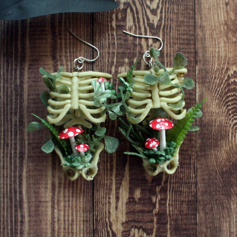 Cottagecore skeleton ribcage torso earrings with plastic greenery and five red and white hand-made polymer clay amanita muscaria mushrooms with sterling silver hooks front view