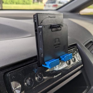 May include: A black car phone mount with the text "Smartphone Holder" and the brand name "Pioneer" printed on it. The mount is attached to a black car stereo with the brand name "Pioneer" printed on it.