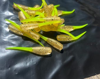 May include: A collection of soft plastic fishing lures. The lures are a translucent gold colour with black flecks and bright neon green tails. The lures are designed to mimic small baitfish.