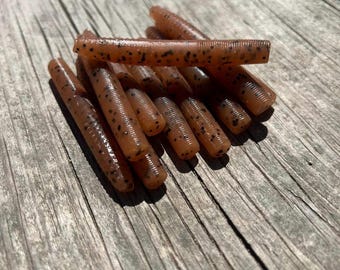 May include: A collection of soft plastic fishing lures. The lures are a translucent brown colour with small black speckles. The lures are cylindrical and appear to be made of a flexible material.