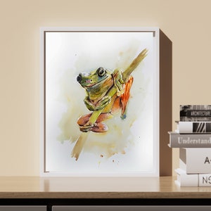 May include: A watercolour painting of a green tree frog sitting on a branch. The frog has orange feet and is looking to the left. The painting is framed in a white frame.