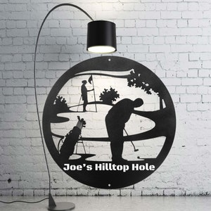 May include: Black metal silhouette of two golfers on a golf course with the text "Joe's Hilltop Hole".