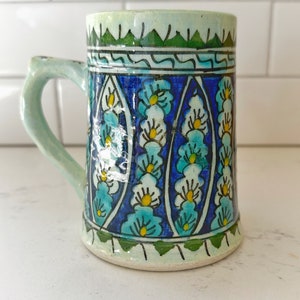 May include: A ceramic mug with a blue and white floral pattern. The mug has a green rim and base.