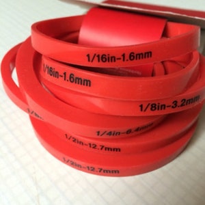 May include: A set of red rubber rings with different sizes marked in inches and millimeters. The sizes are 1/16 inch, 1/8 inch, 1/4 inch, and 1/2 inch.