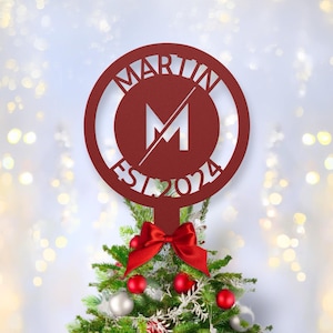 May include: Red metal Christmas tree topper with a circle design. The circle has the text "MARTIN" at the top, the letter "M" in the center, and "EST 2024" at the bottom.