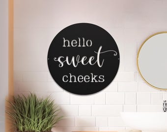 Op de afbeelding: Rond zwart bord met witte tekst die "hello sweet cheeks" zegt.