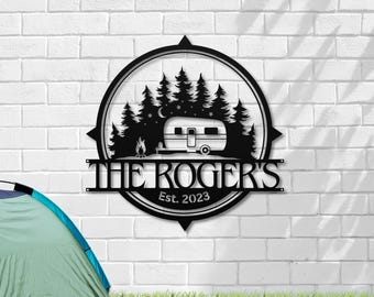 Könnte beinhalten: Schwarzes Metallschild mit Kompass-Design, das eine Silhouette eines Wohnwagens, Bäume und Sterne zeigt. Der Text "The Rogers" und "Est. 2023" ist auf dem Schild zu sehen.