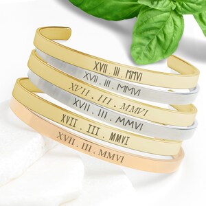 May include: A set of five gold and silver bangle bracelets with Roman numeral and year engravings. The bracelets are stacked on top of each other.