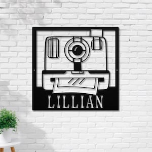 May include: Black metal wall art featuring a vintage camera with a film strip and the name "Lillian" below.
