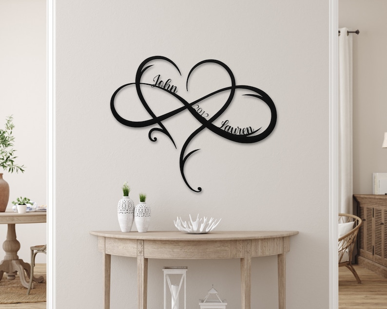 May include: Black metal infinity symbol wall art with a heart in the center. The names "John" and "Lauren" are written on either side of the heart, with the year "2012" written above the heart.