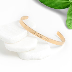 May include: Gold bangle bracelet with a delicate inscription that reads "J ♥ M" with a small heart and a star.