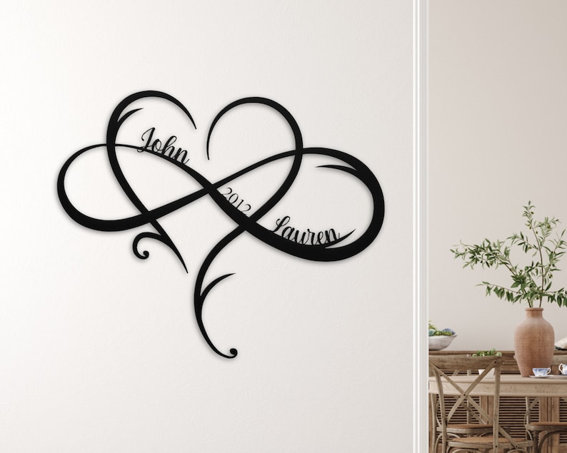 May include: Black metal wall art featuring an infinity symbol intertwined with a heart. The names "John" and "Lauren" and the year "2012" are inscribed within the design.