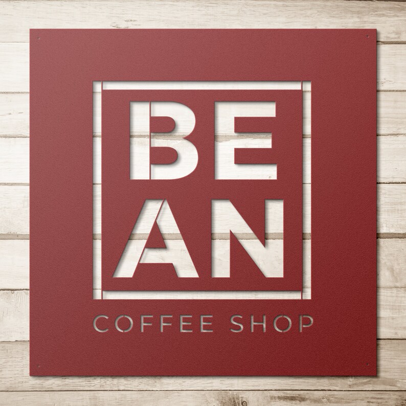 K&ouml;nnte beinhalten: Ein rotes Metallschild mit den Worten "BE AN COFFEE SHOP" in wei&szlig; ausgeschnitten. Das Schild hat einen rustikalen, Vintage-Look.